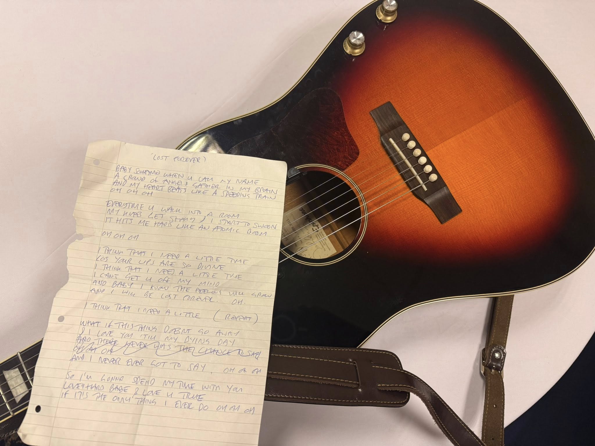 Photo showing an acoustic guitar with a handwritten lyric sheet over the fretboard